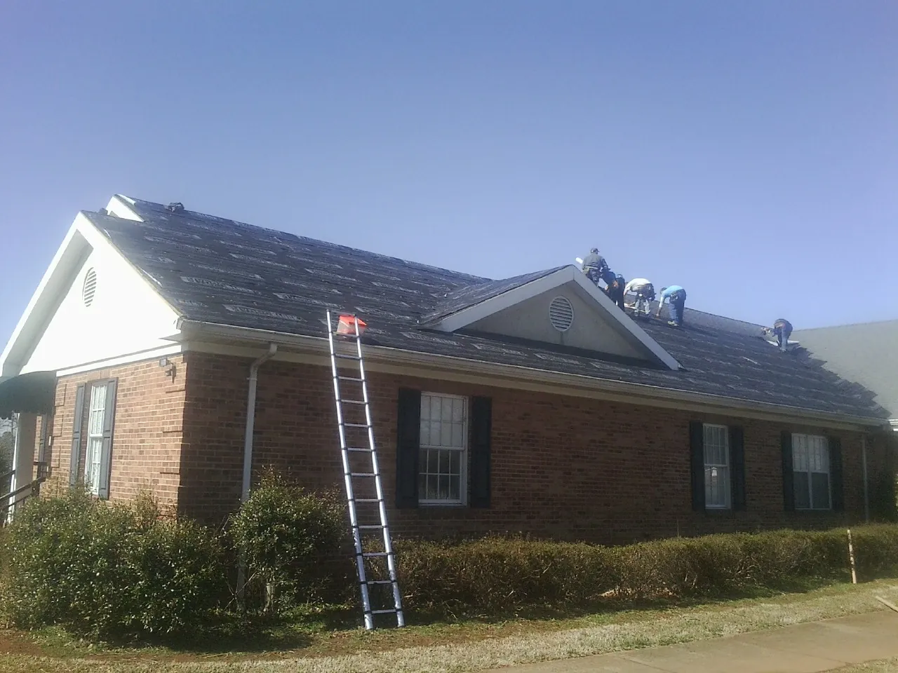 Crew tearing shingles off a brick ranch roof with a ladder set — Metal Roof Repair work by our crew in Edison